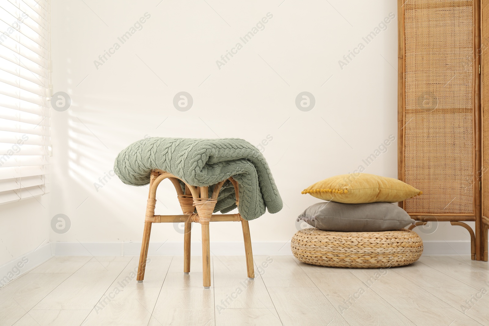 Green woolen blanket on stool and pillows indoors Photo of Green woolen blanket on stool and pillows indoors
