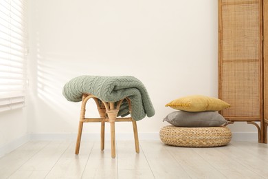 Photo of Green woolen blanket on stool and pillows indoors