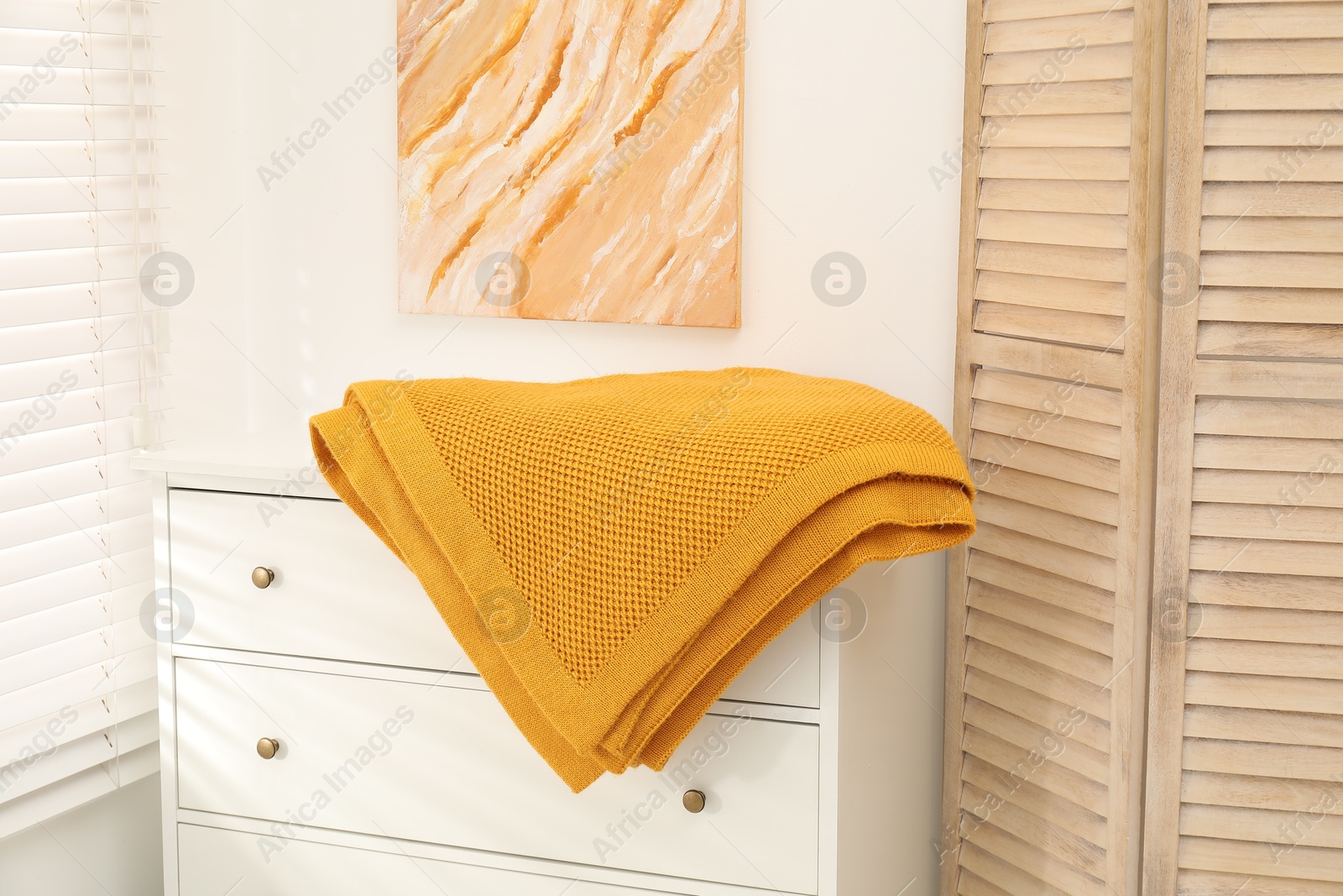 Orange woolen blanket on white chest of drawers indoors Photo of Orange woolen blanket on white chest of drawers indoors