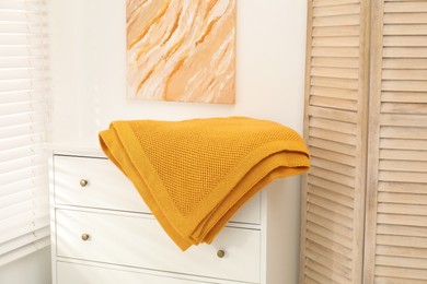 Photo of Orange woolen blanket on white chest of drawers indoors