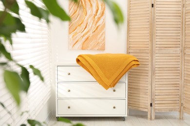 Photo of Orange woolen blanket on white chest of drawers indoors