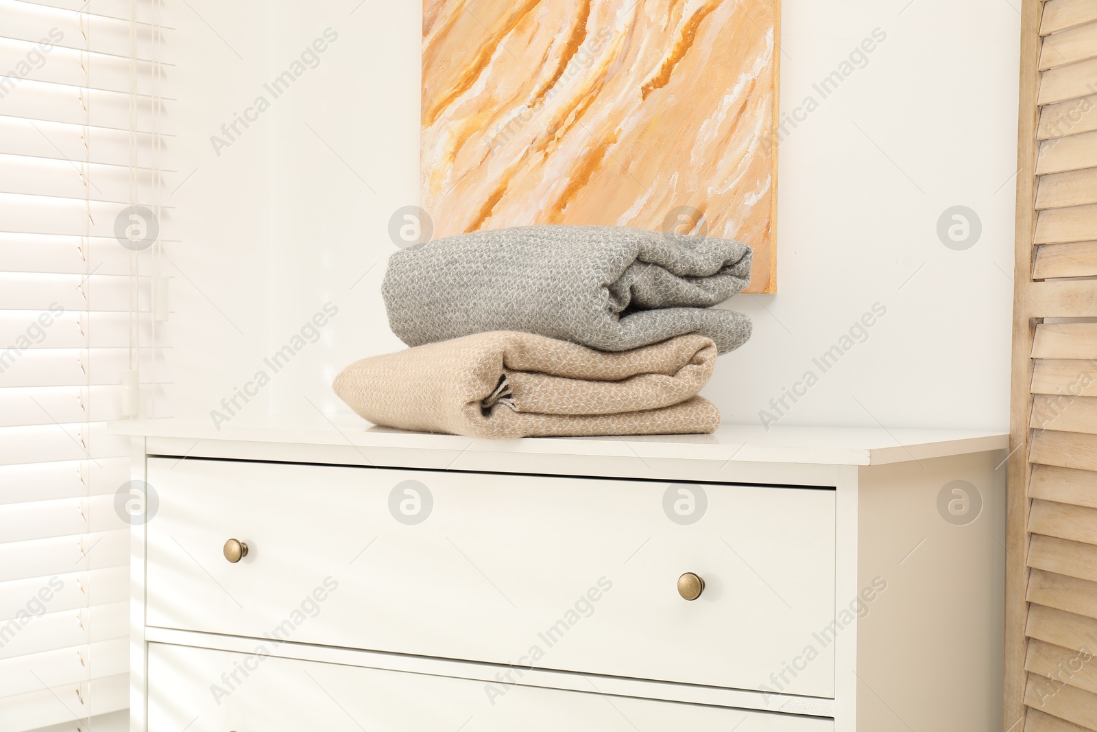 Woolen blankets on white chest of drawers indoors Photo of Woolen blankets on white chest of drawers indoors
