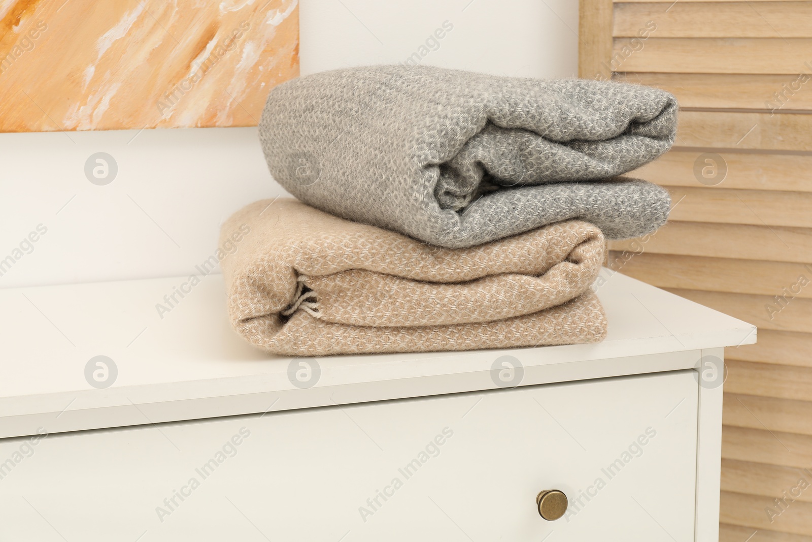Woolen blankets on white chest of drawers indoors Photo of Woolen blankets on white chest of drawers indoors