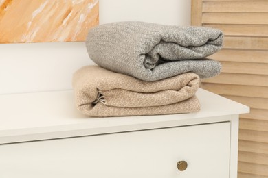 Photo of Woolen blankets on white chest of drawers indoors