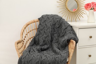 Photo of Wicker chair with gray woolen blanket and decor chest of drawers near white wall indoors