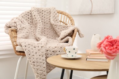Photo of Wicker chair with woolen blanket, books, vase and cup on wooden table indoors