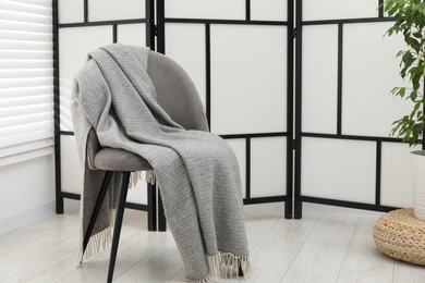Photo of Comfortable armchair with gray woolen blanket indoors