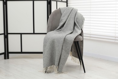 Photo of Comfortable armchair with gray woolen blanket indoors