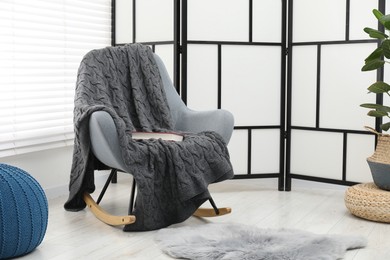 Photo of Comfortable armchair with gray woolen blanket and book indoors