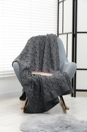 Photo of Comfortable armchair with gray woolen blanket and book indoors