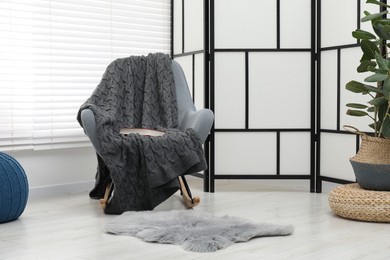 Photo of Comfortable armchair with gray woolen blanket and book indoors