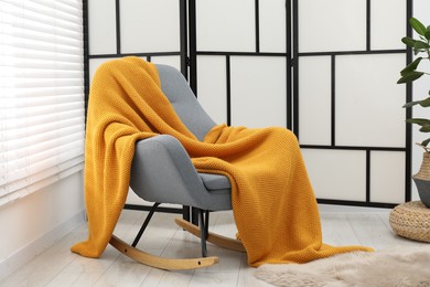 Photo of Comfortable armchair with orange woolen blanket indoors