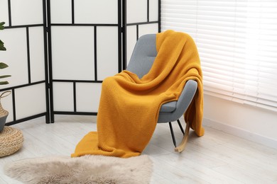 Photo of Comfortable armchair with orange woolen blanket indoors