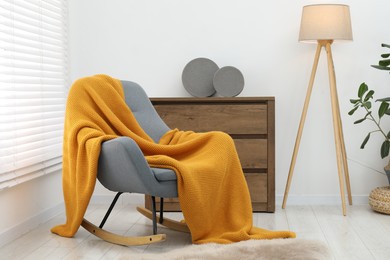 Photo of Comfortable armchair with orange woolen blanket indoors