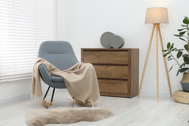 Photo of Comfortable armchair with beige woolen blanket indoors