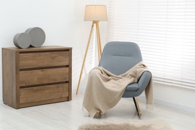 Photo of Comfortable armchair with beige woolen blanket indoors