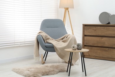 Photo of Comfortable armchair with beige woolen blanket and decor on wooden table indoors