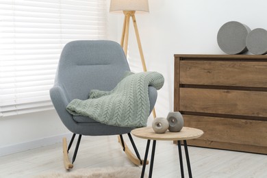 Photo of Comfortable armchair with green woolen blanket and decor on wooden table indoors