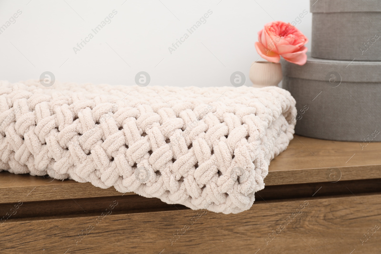 Woolen blanket, boxes and beautiful flower in vase on wooden chest near white wall indoors, closeup Photo of Woolen blanket, boxes and beautiful flower in vase on wooden chest near white wall indoors, closeup