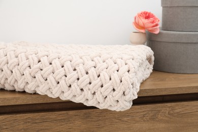 Photo of Woolen blanket, boxes and beautiful flower in vase on wooden chest near white wall indoors, closeup