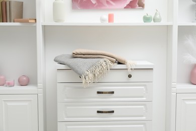 Photo of Woolen blankets on white chest of drawers indoors