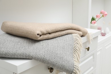 Photo of Woolen blankets on white chest of drawers indoors, closeup
