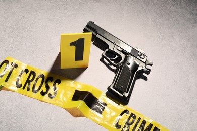 Photo of Forensic expertise. Crime scene tape and gun on light grey background, top view