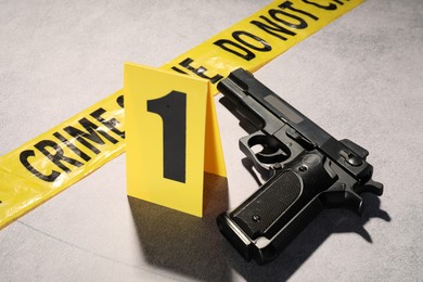 Photo of Forensic expertise. Crime scene tape and gun on light grey background, closeup