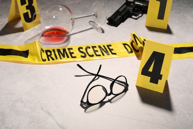 Photo of Forensic expertise. Crime scene with evidence, markers and police tape on light grey background, closeup