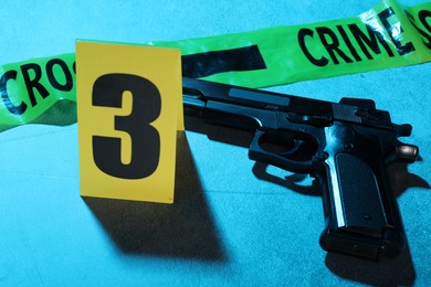 Photo of Forensic expertise. Crime scene tape and gun on blue background, closeup. Color toned effect