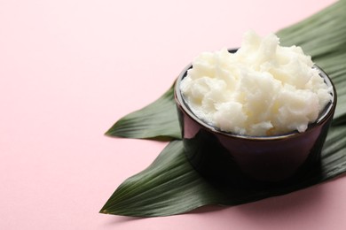 Photo of Natural shea butter and leaves on pink background, closeup. Space for text