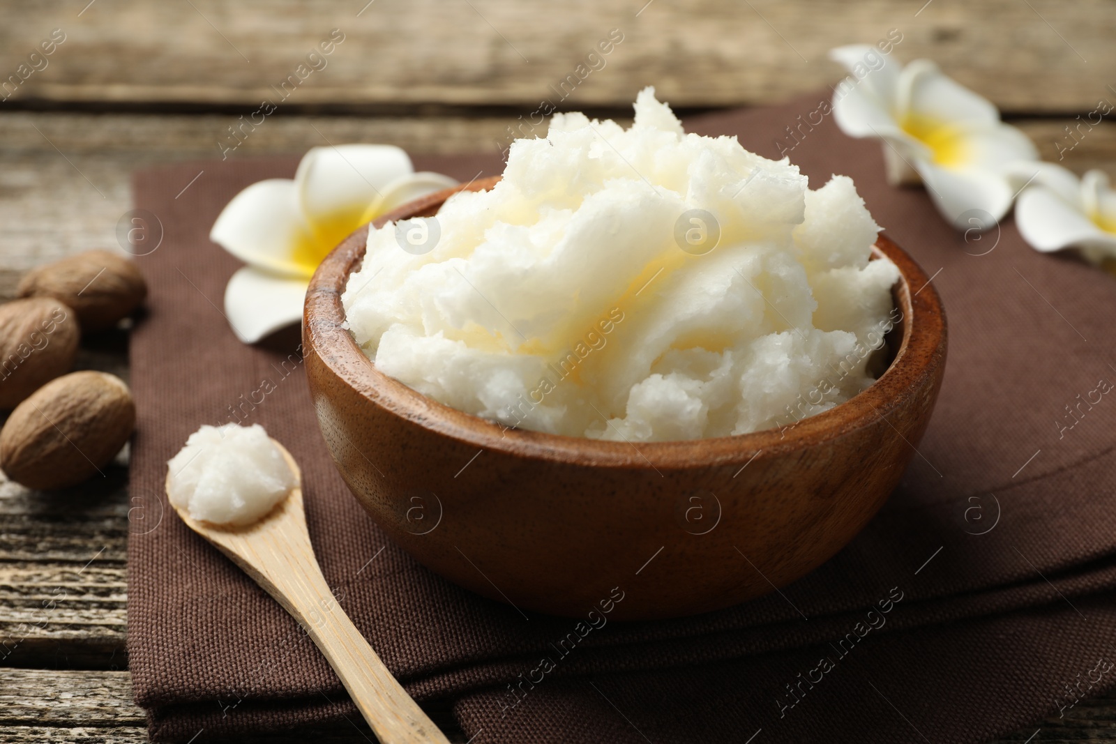 Photo of Natural shea butter and plumeria flowers on wooden table, closeup