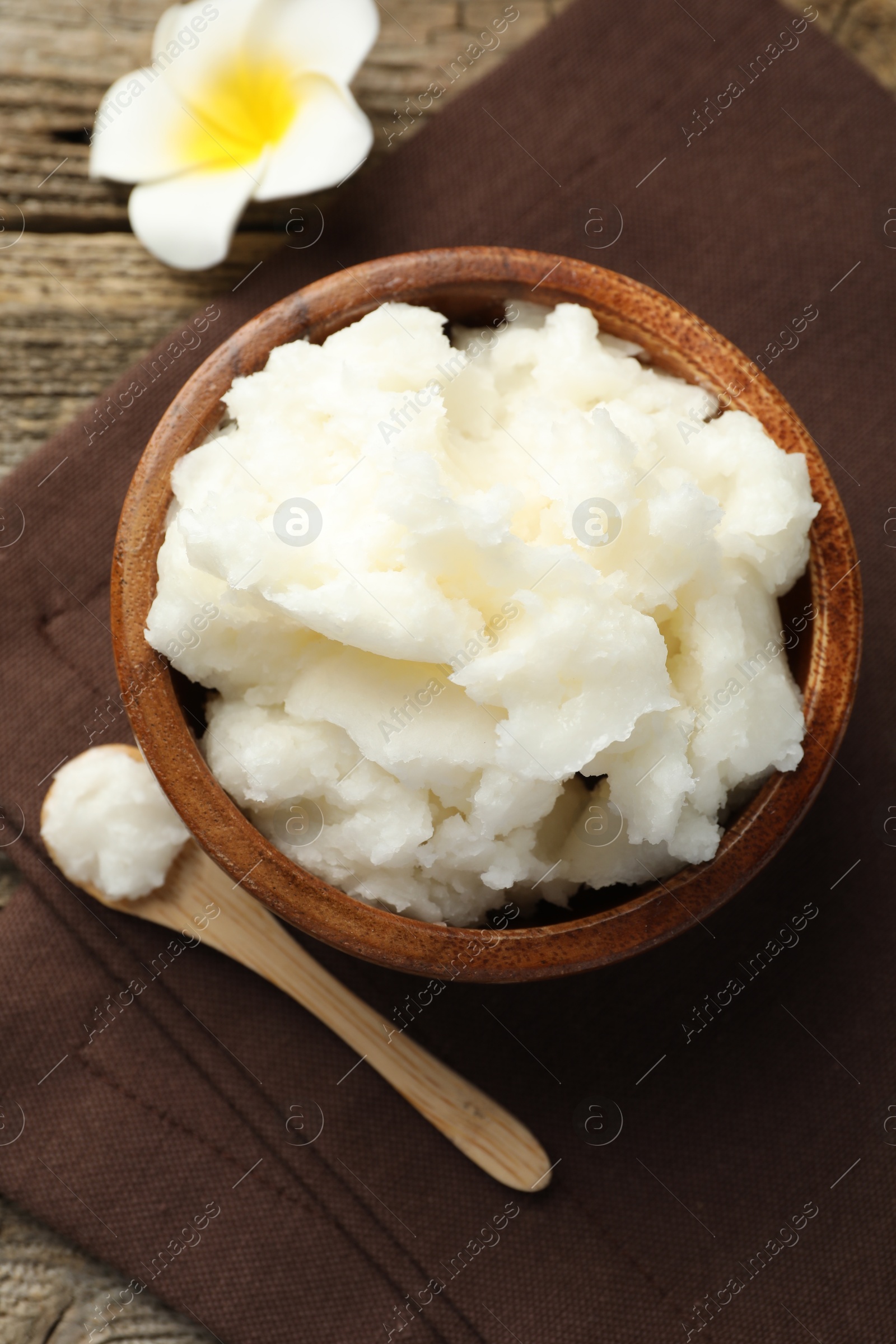 Photo of Natural shea butter and plumeria flower on wooden table, flat lay