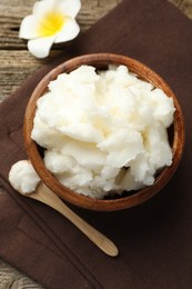 Photo of Natural shea butter and plumeria flower on wooden table, flat lay