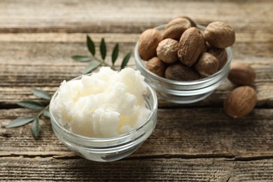 Photo of Natural shea butter, nuts and leaves on wooden table, closeup