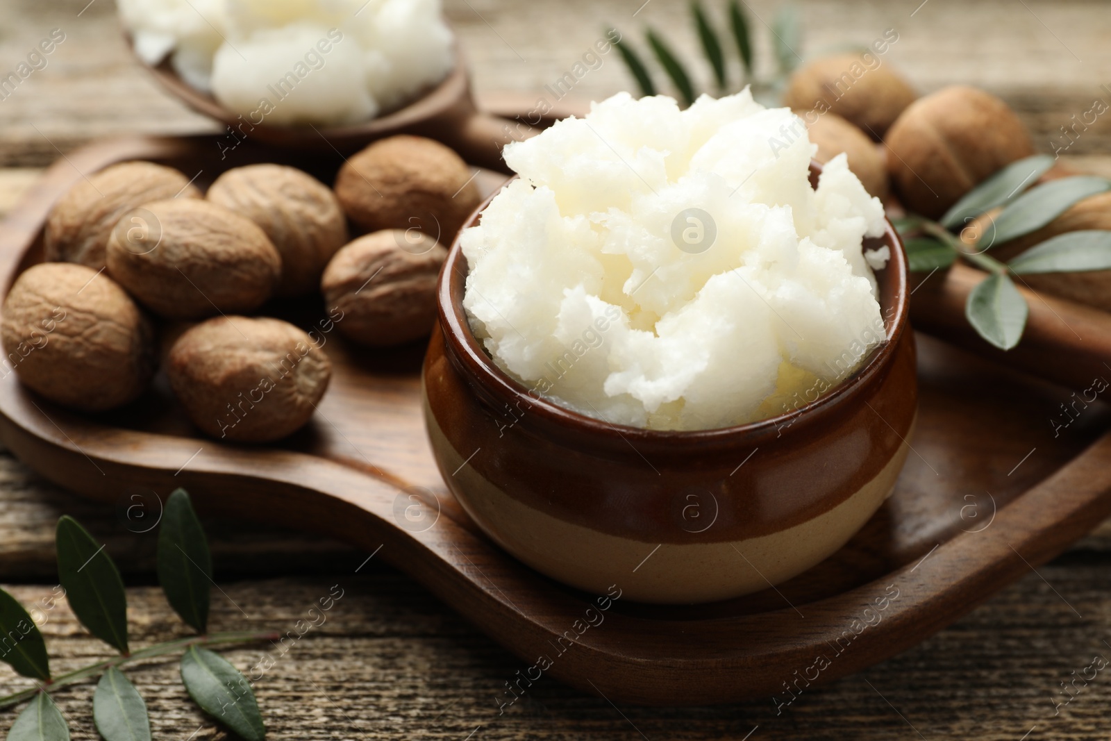 Natural shea butter, nuts and leaves on wooden table, closeup Photo of Natural shea butter, nuts and leaves on wooden table, closeup