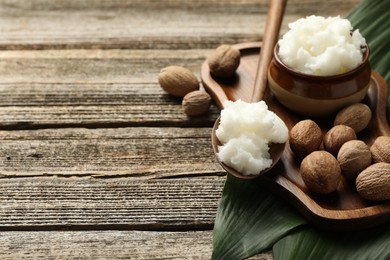 Photo of Natural shea butter, nuts and leaves on wooden table, closeup. Space for text