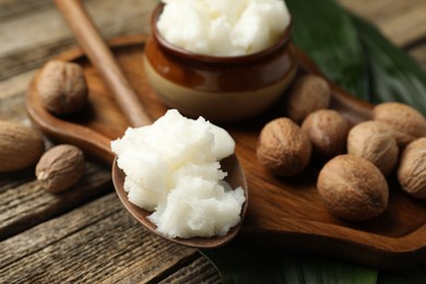 Photo of Natural shea butter, nuts and leaves on wooden table, closeup
