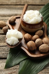 Photo of Natural shea butter, nuts and leaves on wooden table, closeup