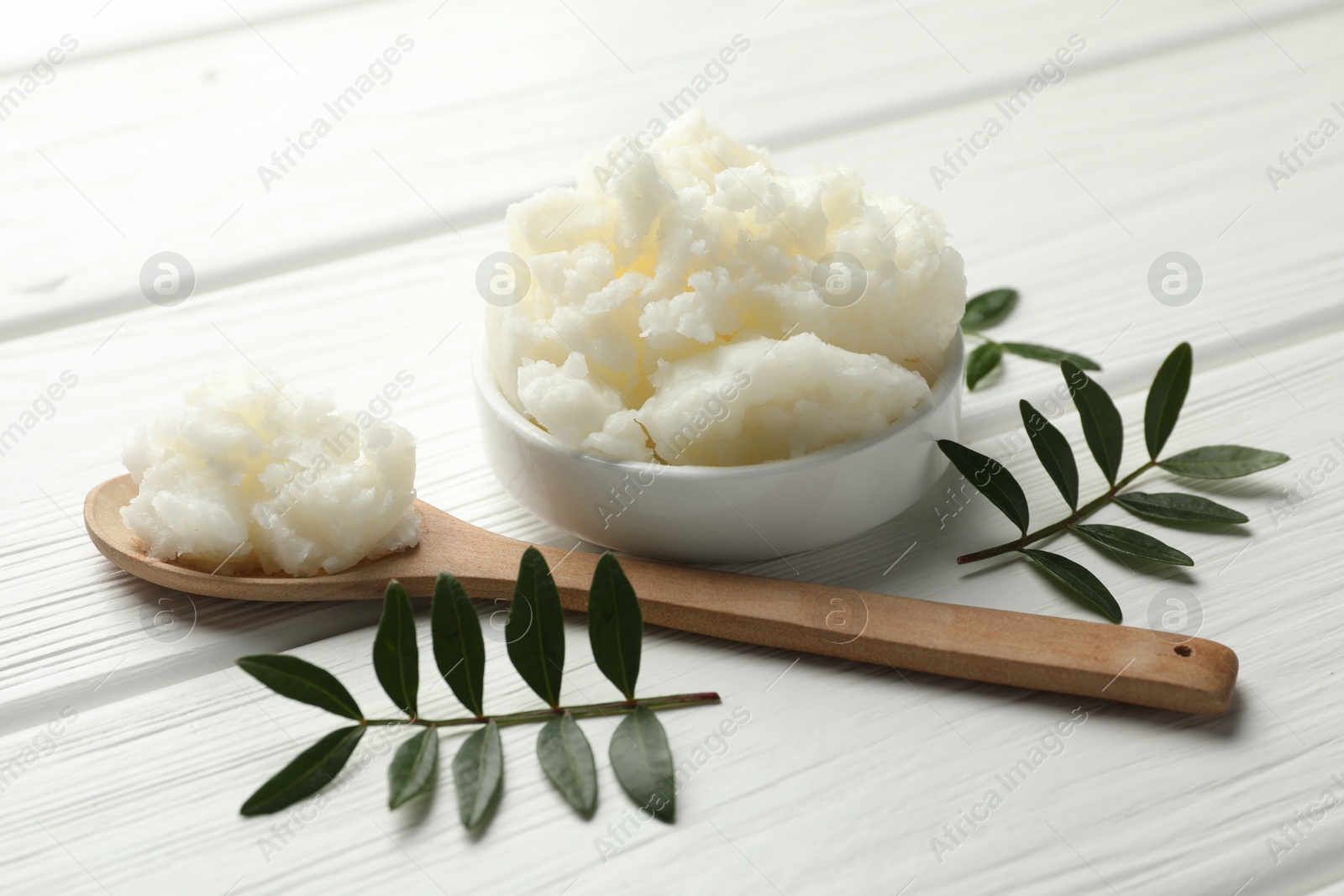 Photo of Natural shea butter and leaves on white wooden table, closeup