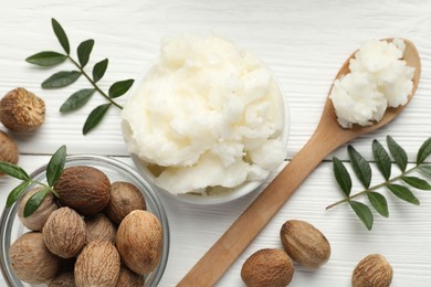 Photo of Natural shea butter, nuts and leaves on white wooden table, flat lay