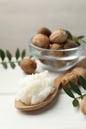Photo of Natural shea butter, nuts and leaves on white wooden table, closeup