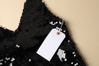Photo of Stylish dress with tag and sequins on beige background, top view