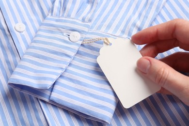 Photo of Woman holding tag of striped shirt, closeup