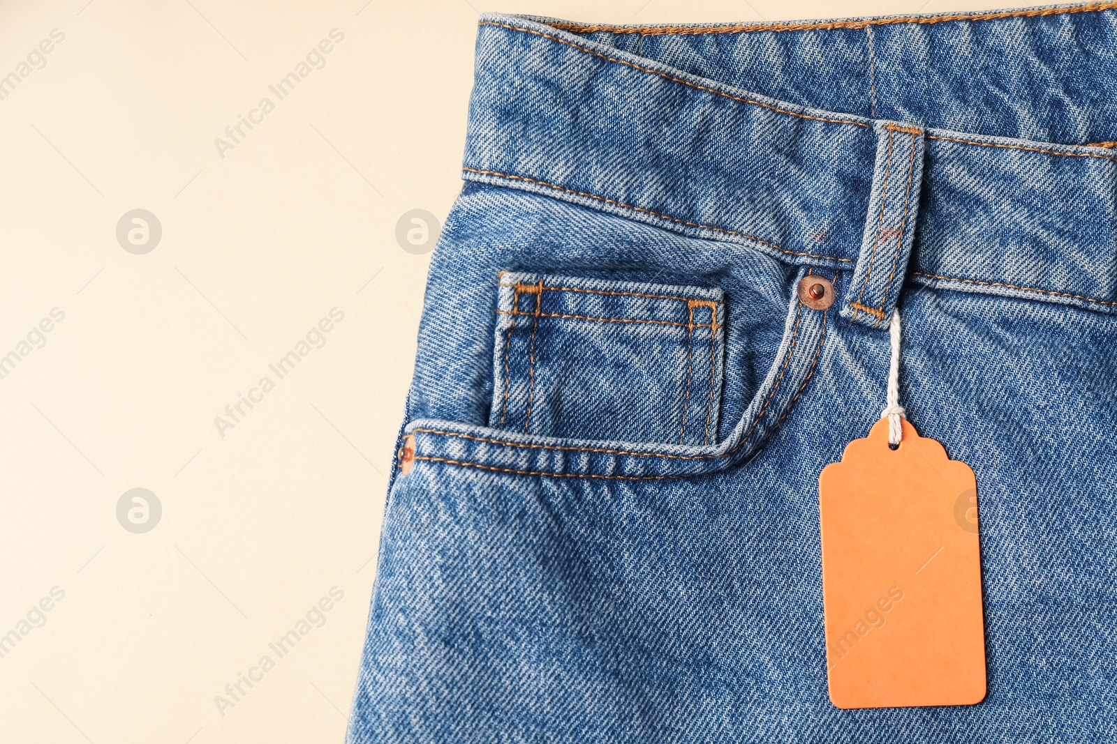 Blue jeans with tag on beige background, top view. Space for text Photo of Blue jeans with tag on beige background, top view. Space for text