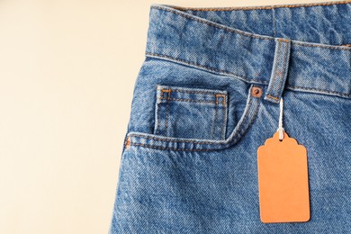 Photo of Blue jeans with tag on beige background, top view. Space for text