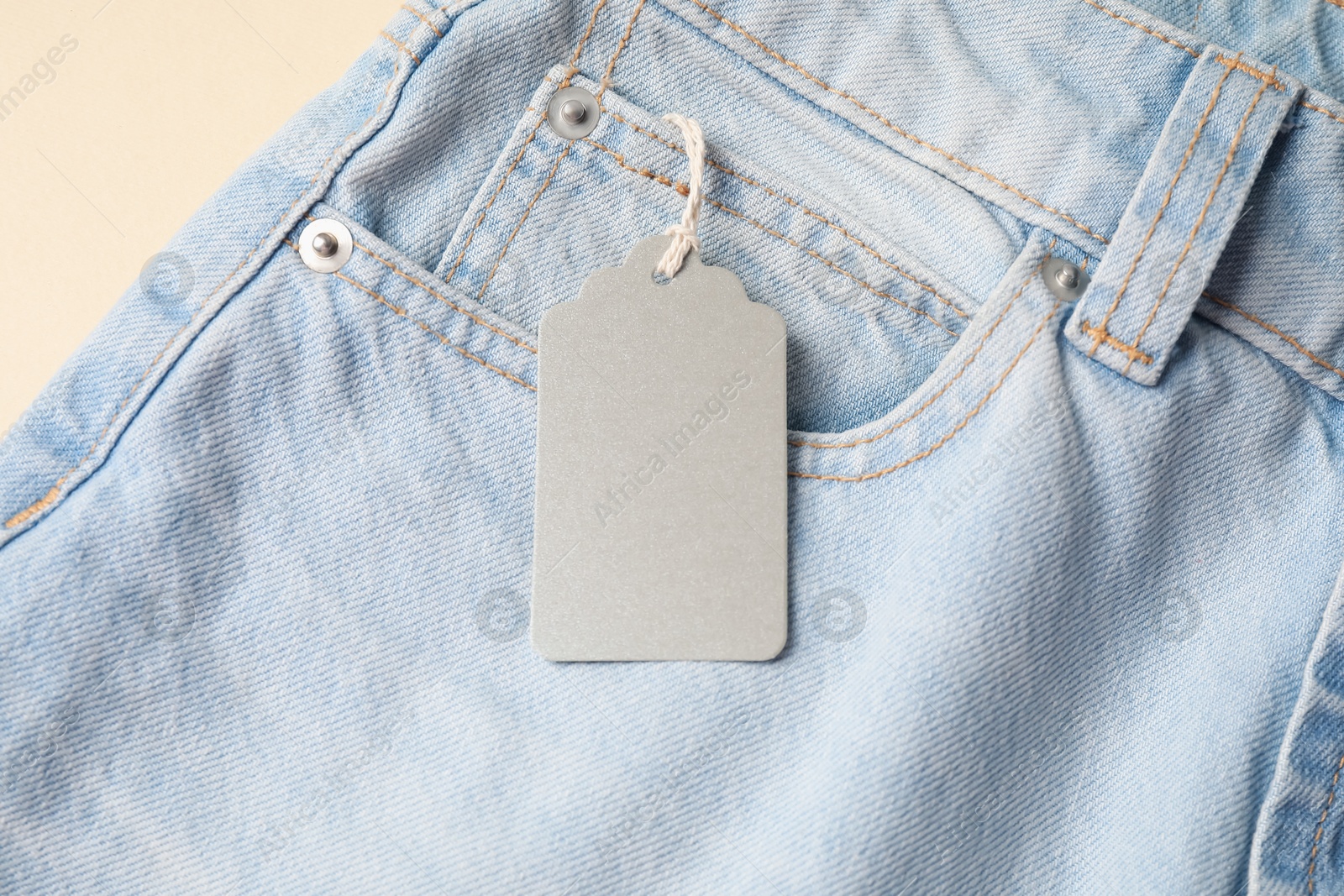 Light blue jeans with tag on beige background, above view Photo of Light blue jeans with tag on beige background, above view
