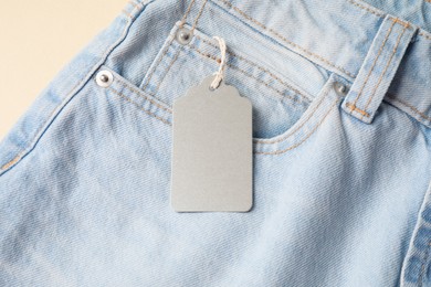 Photo of Light blue jeans with tag on beige background, above view