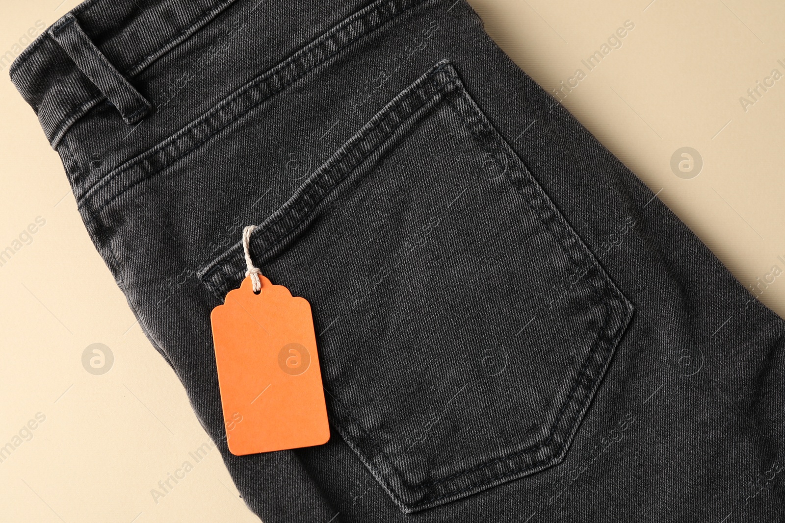 Black jeans with tag on beige background, top view Photo of Black jeans with tag on beige background, top view