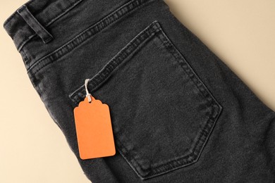 Photo of Black jeans with tag on beige background, top view